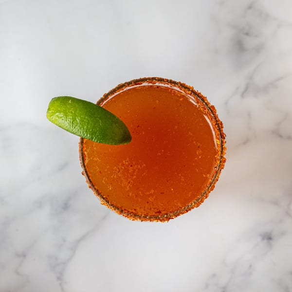 Overhead view of a Cafe La Taza michelada with a chili-salted rim and a lime wedge.