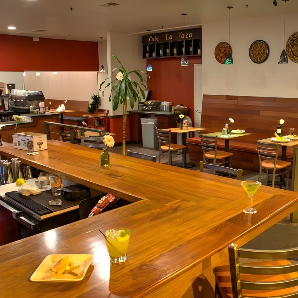 Cafe La Taza's interior with a long wooden bar, dining tables, and a coffee station.