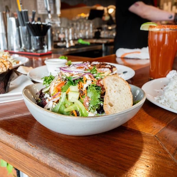 A fresh salad with mixed greens, red onion, and bread, next to a red drink at Cafe La Taza.