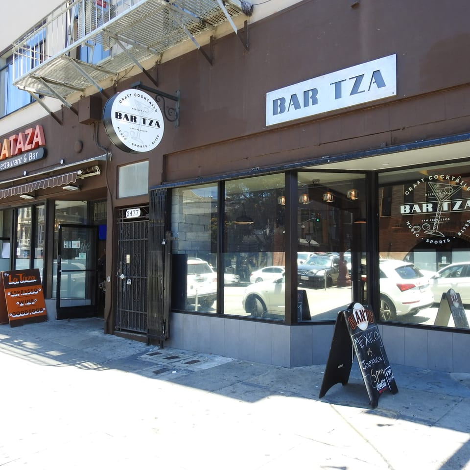 Exterior of Bar Tza, a bar and restaurant with large windows and a round sign.