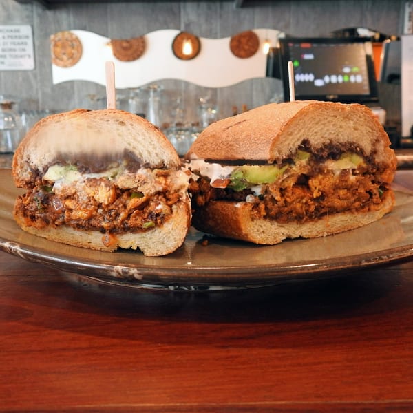 Two halves of a Cafe La Taza sandwich filled with meat, avocado, and sauce on a plate.