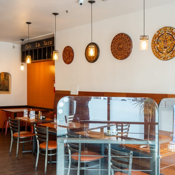 Cafe La Taza interior with wooden tables, chairs, decorative wall plates, and hanging pendant lights.