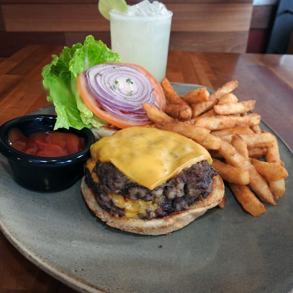A double cheeseburger with lettuce, tomato, and onion, served with fries, ketchup, and a drink.